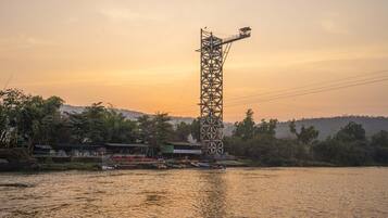 A tall metal structure by a river with boats and buildings in the background.