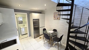 A modern kitchen with a glass dining table, a refrigerator, and a staircase.
