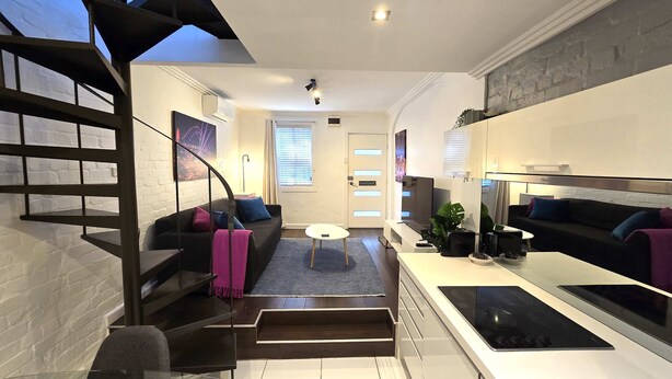A modern living room with a staircase, a sofa, a coffee table, and a kitchen area with a stove.