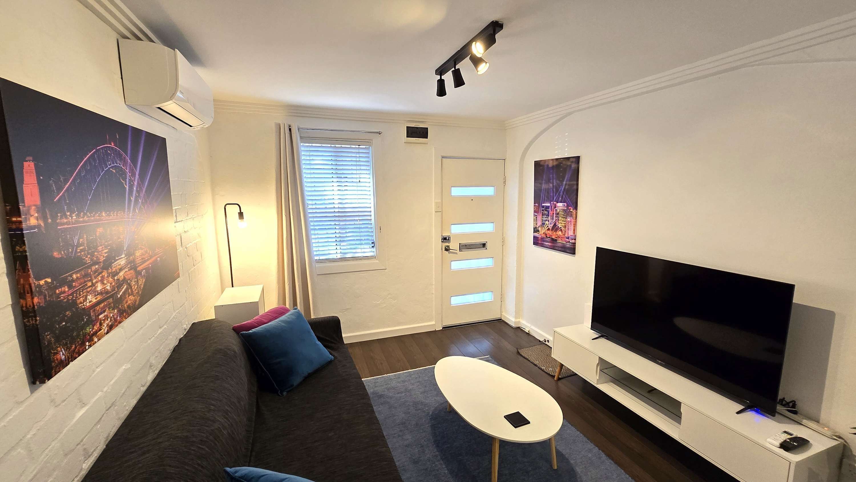Un salon moderne avec un téléviseur à écran plat, un canapé, une table basse et des œuvres d’art accrochées aux murs.