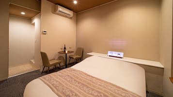 Ett hotellrum med en säng, ett litet bord med stolar, en luftkonditioneringsanläggning och en kontrollpanel på väggen.