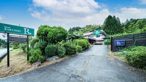 Ein Weg führt zum Hotel Rakuseki R, umgeben von üppigem Grün und einer Berglandschaft im Hintergrund.