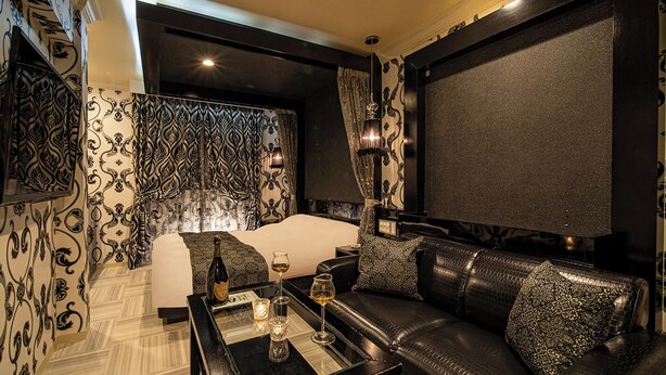 Ein luxuriöses Zimmer mit einem großen Bett, einem Ledersofa und einem kleinen Tisch mit einer Flasche und Gläsern.