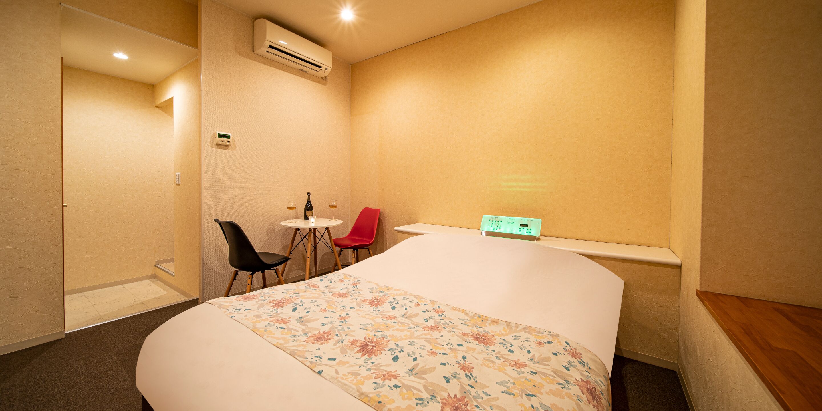 Ein Hotelzimmer mit einem großen Bett, einem kleinen Tisch mit zwei Stühlen, einer Klimaanlage und einer Steckdose an der Wand.