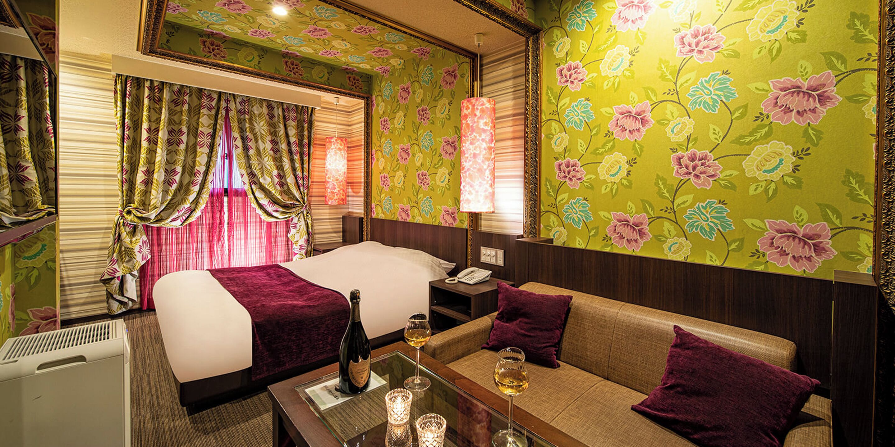 A hotel room with a bed, a sofa, a table with a bottle and glass, and a telephone.