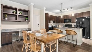 A modern kitchen with dark wooden cabinets, a central island with bar stools, a built-in microwave, and a black refrigerator. - Modish Keen King Bed w/ Pool (Houston)