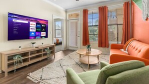 A living room with a flat-screen TV mounted on the wall, a ceiling fan, a wooden console table, a round coffee table, and a sofa. - Modish Keen King Bed w/ Pool (Houston)