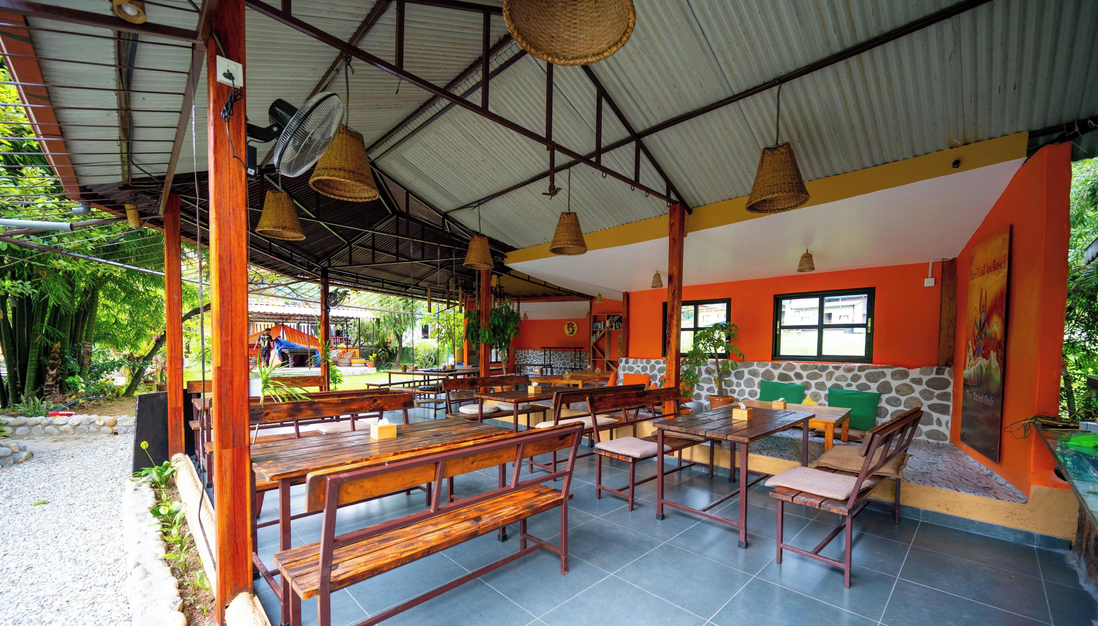 Un restaurante al aire libre con bancos y mesas de madera, techo de metal corrugado y pared de piedra.