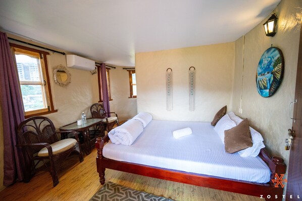 A hotel room with a wooden bed, a dining table with chairs, a small table with a bottle, and a window with curtains. - Zostel Pokhara (Pokhara)