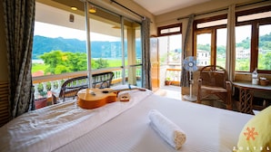 A hotel room with a large bed, a guitar, a fan, and a view of a mountain and greenery. - Zostel Pokhara (Pokhara)