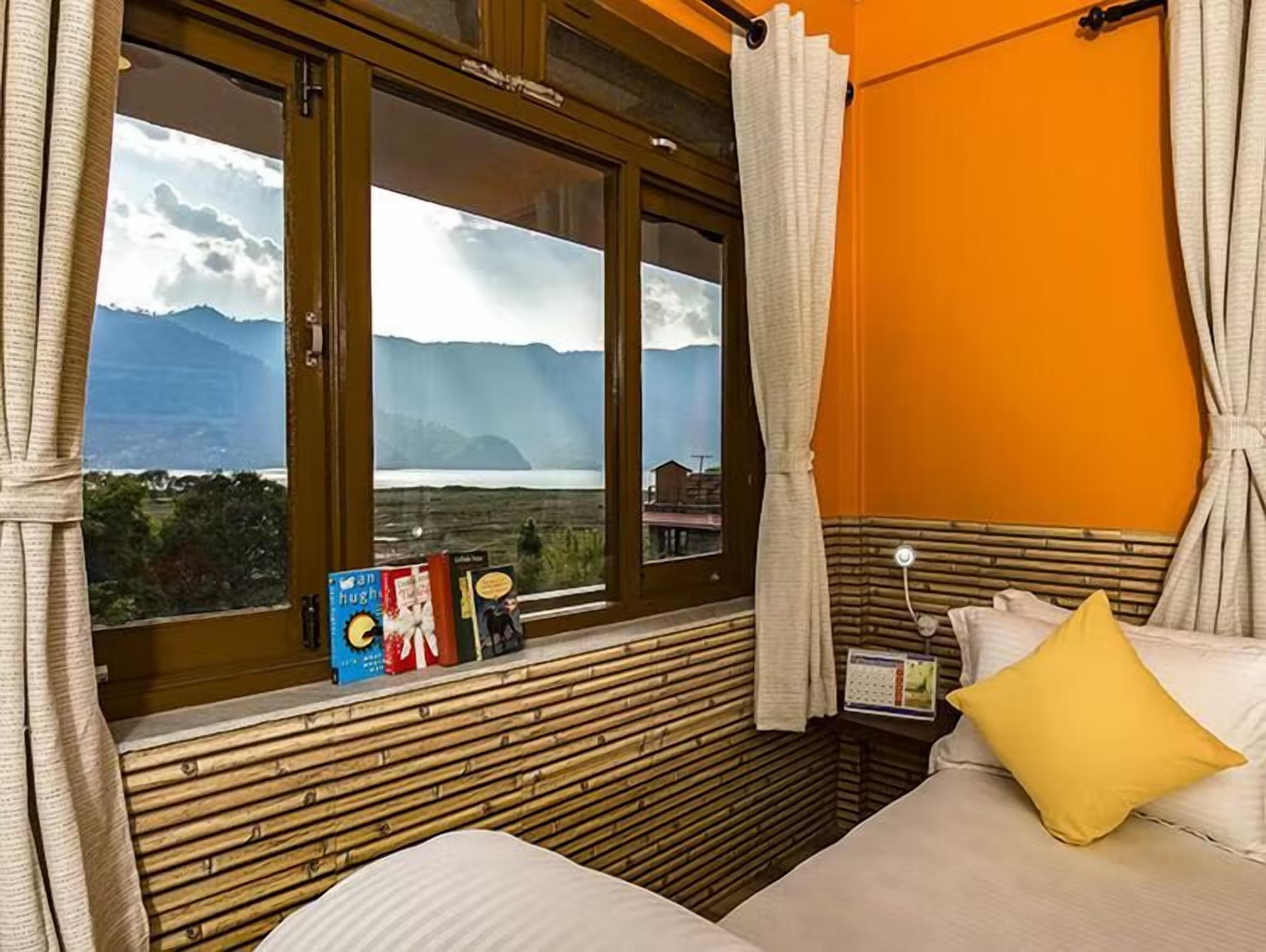 Une chambre avec un lit, une fenêtre avec des rideaux, une tête de lit en bois et une vue sur les montagnes.