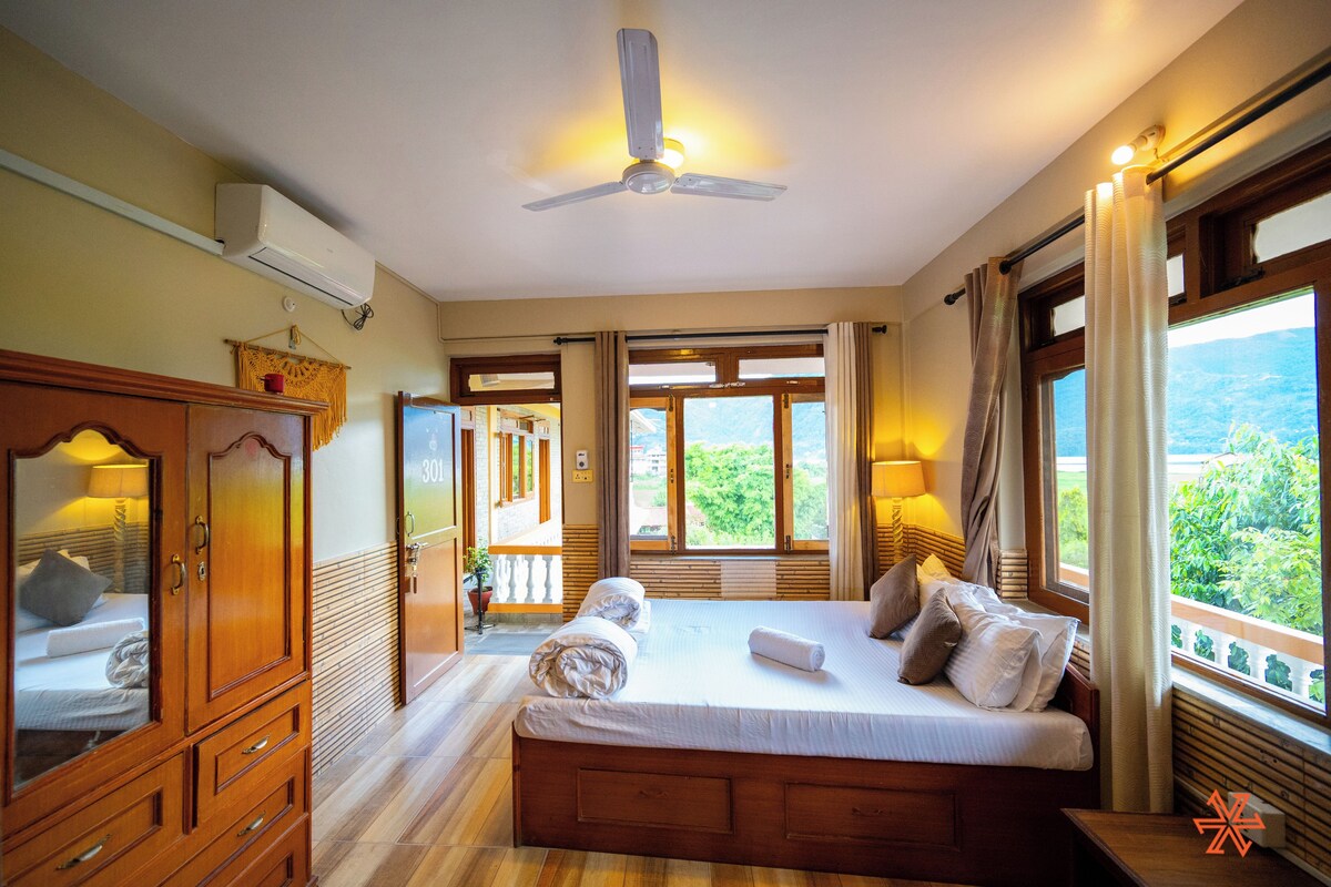 A bedroom with a large bed, wooden furniture, and a view of greenery outside.
