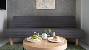 A modern living room with a grey sofa, a round wooden coffee table, and two plates with sandwiches and a plant. - MINI HOUSE Tokyo South (Tokyo)