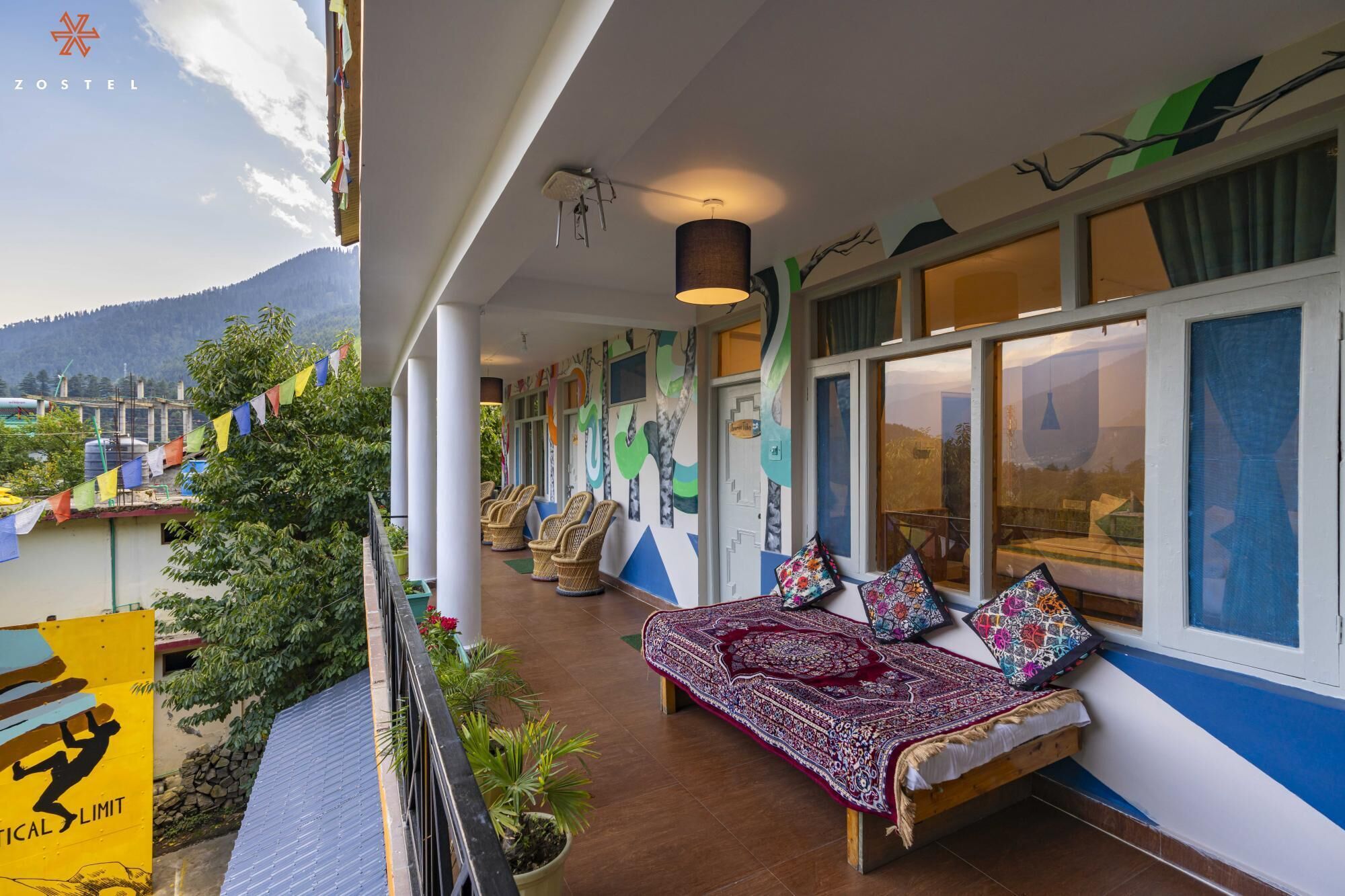 A balcony with wicker chairs, a patterned bed, and a view of mountains.