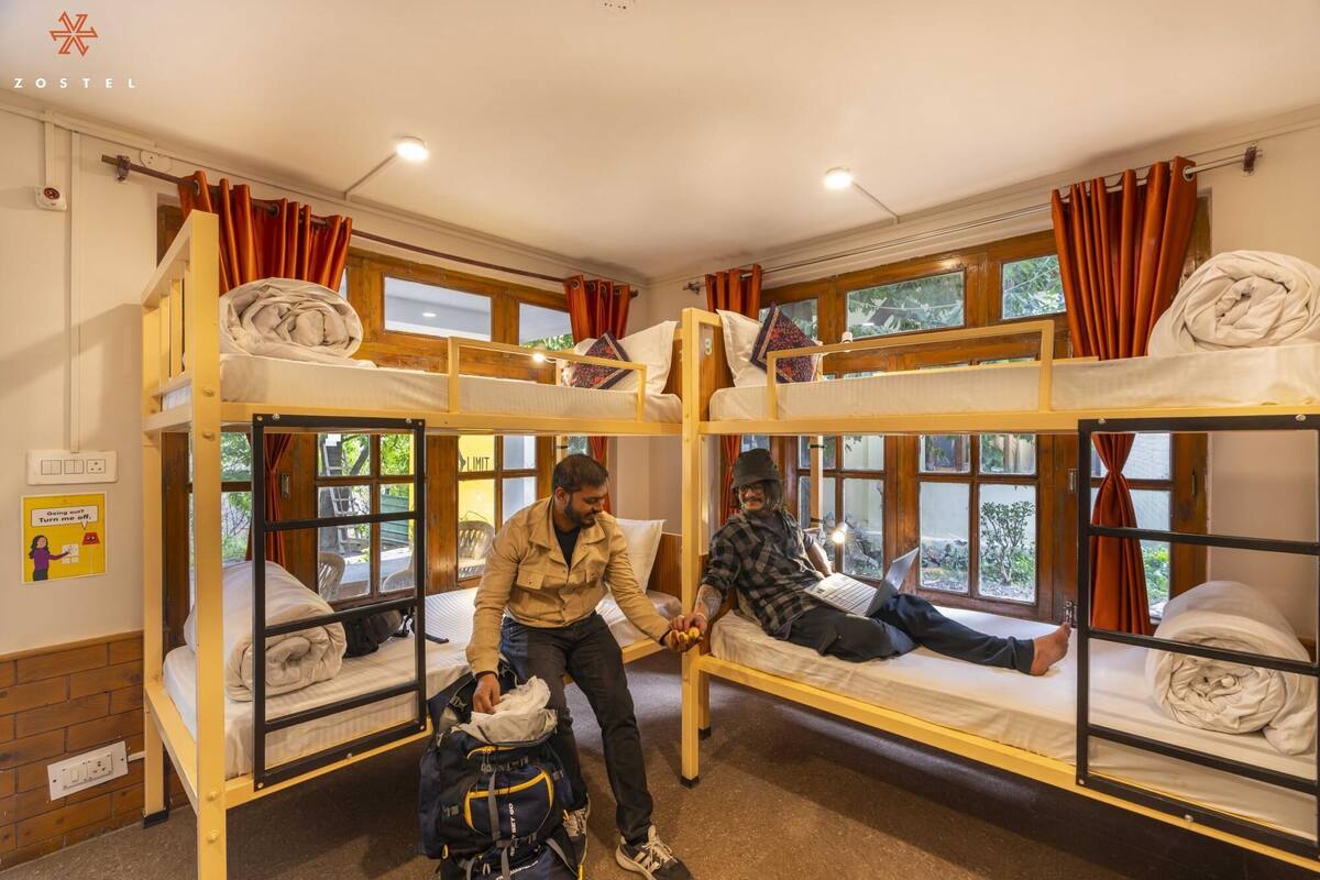 A dormitory room with bunk beds, wooden walls, and large windows with curtains.