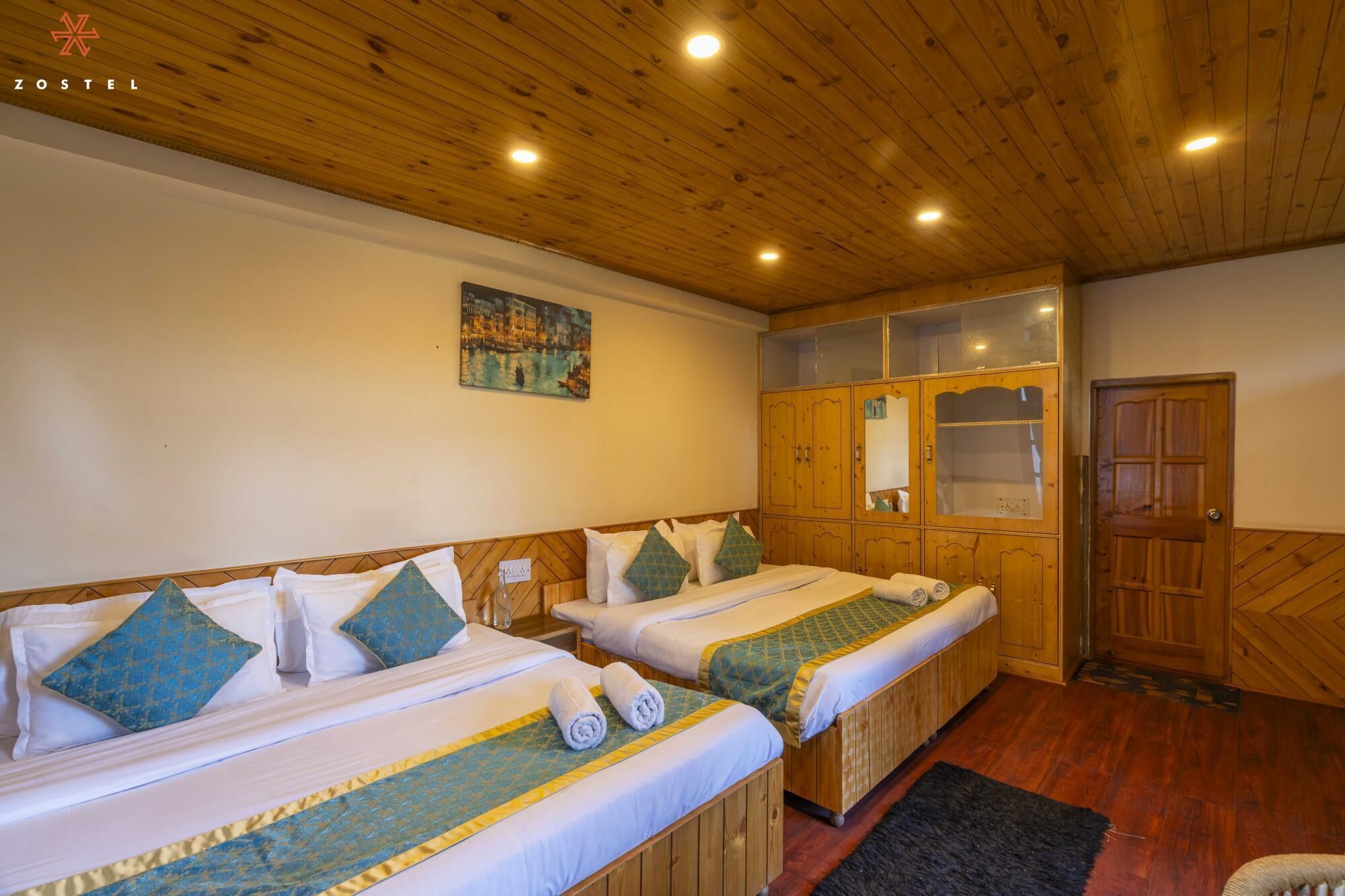A hotel room with two beds, wooden headboards, a large mirror, and a wooden wardrobe.