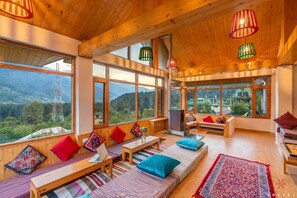 A cozy room with large windows, wooden furniture, and colorful cushions. - Zostel Old Manali (Manali)