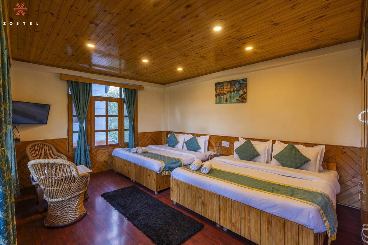 A room with two beds, a television, a wicker chair, and a window with curtains.