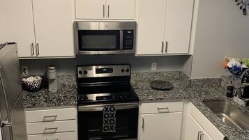 A modern kitchen with white cabinets, stainless steel appliances, granite countertops, and two black kitchen mats with text.
