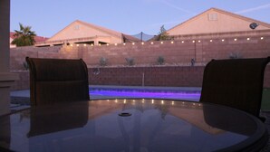 Een terras met een glazen tafel en twee stoelen, een bakstenen muur en een zwembad met blauwe verlichting.