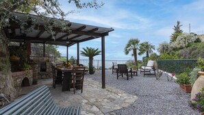 En udendørs terrasse med stenbelægning, et pergolaområde, siddepladser og havudsigt.