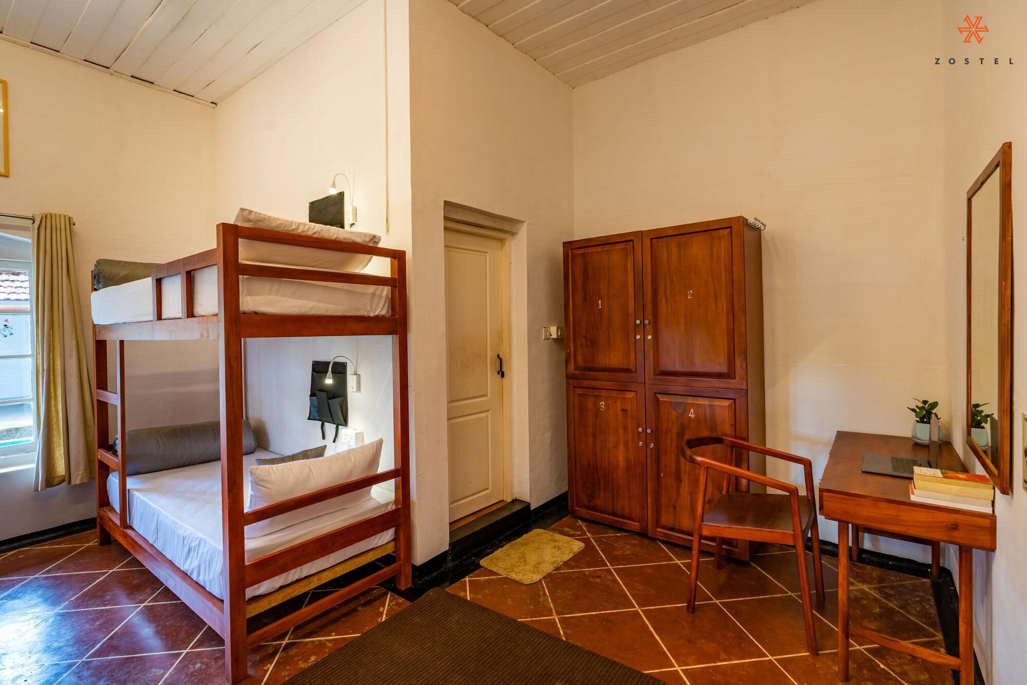 A bunk bed with a desk and chair, wooden wardrobe, and a mirror.