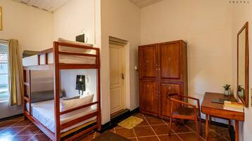 A bunk bed with a desk and chair, wooden wardrobe, and a mirror.