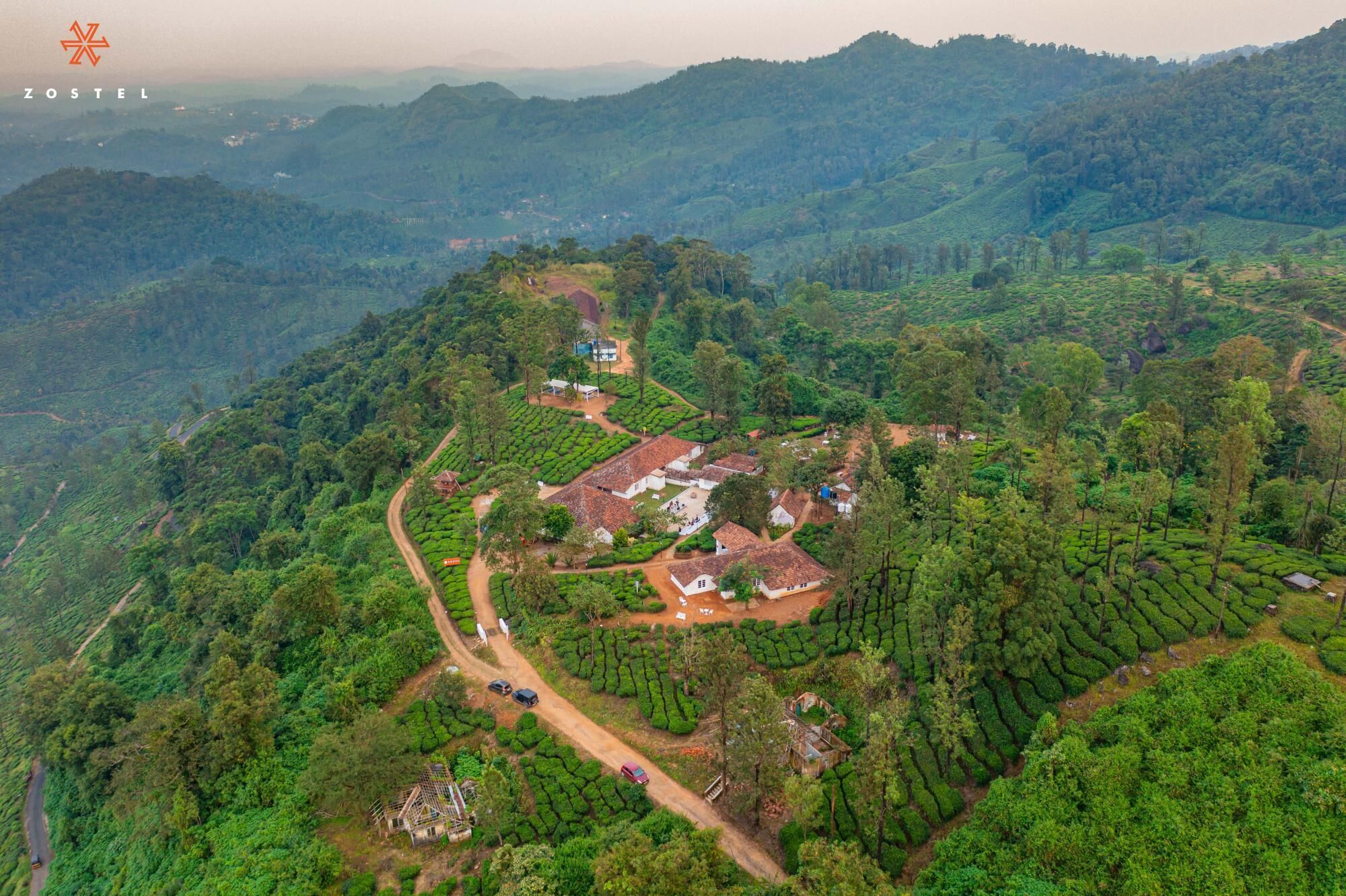 An aerial view of a hilly area with terraced tea plantations and scattered buildings.