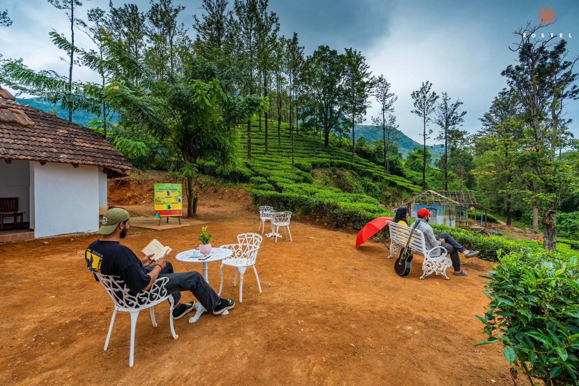 Un espace extérieur aménagé dans un style rustique, avec des chaises et des tables en métal blanc, entouré d’une végétation luxuriante et de collines en terrasses.