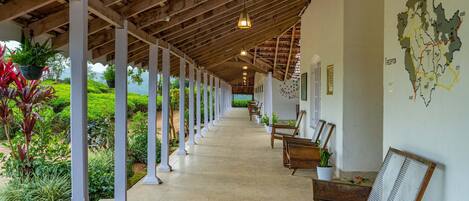 Un corredor cubierto con vigas y columnas de madera, plantas en macetas y zonas de estar.