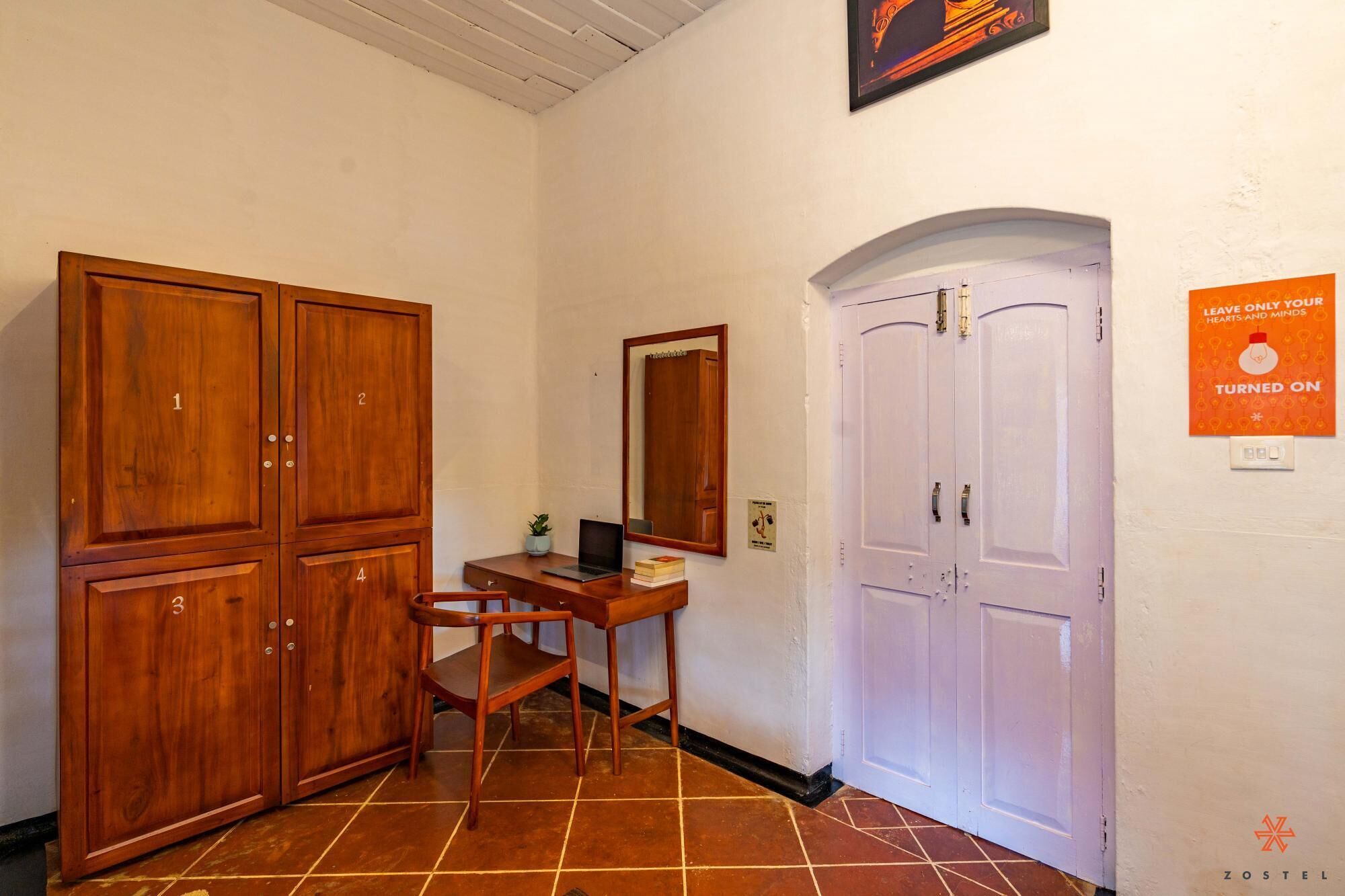 A hallway with wooden cabinets numbered 1 to 4, a desk with a laptop, a mirror, and a door with a sign.