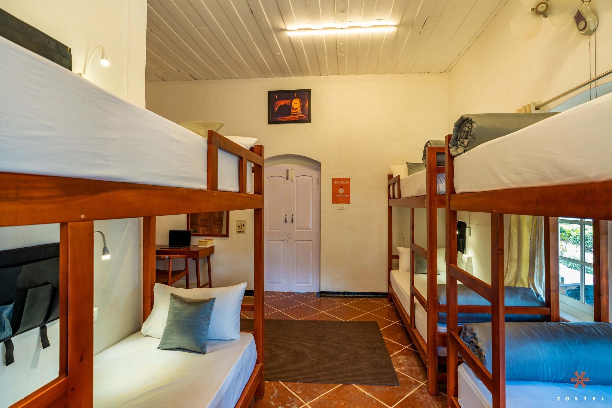 A dormitory room with bunk beds, a desk with a laptop, and a door with a sign.