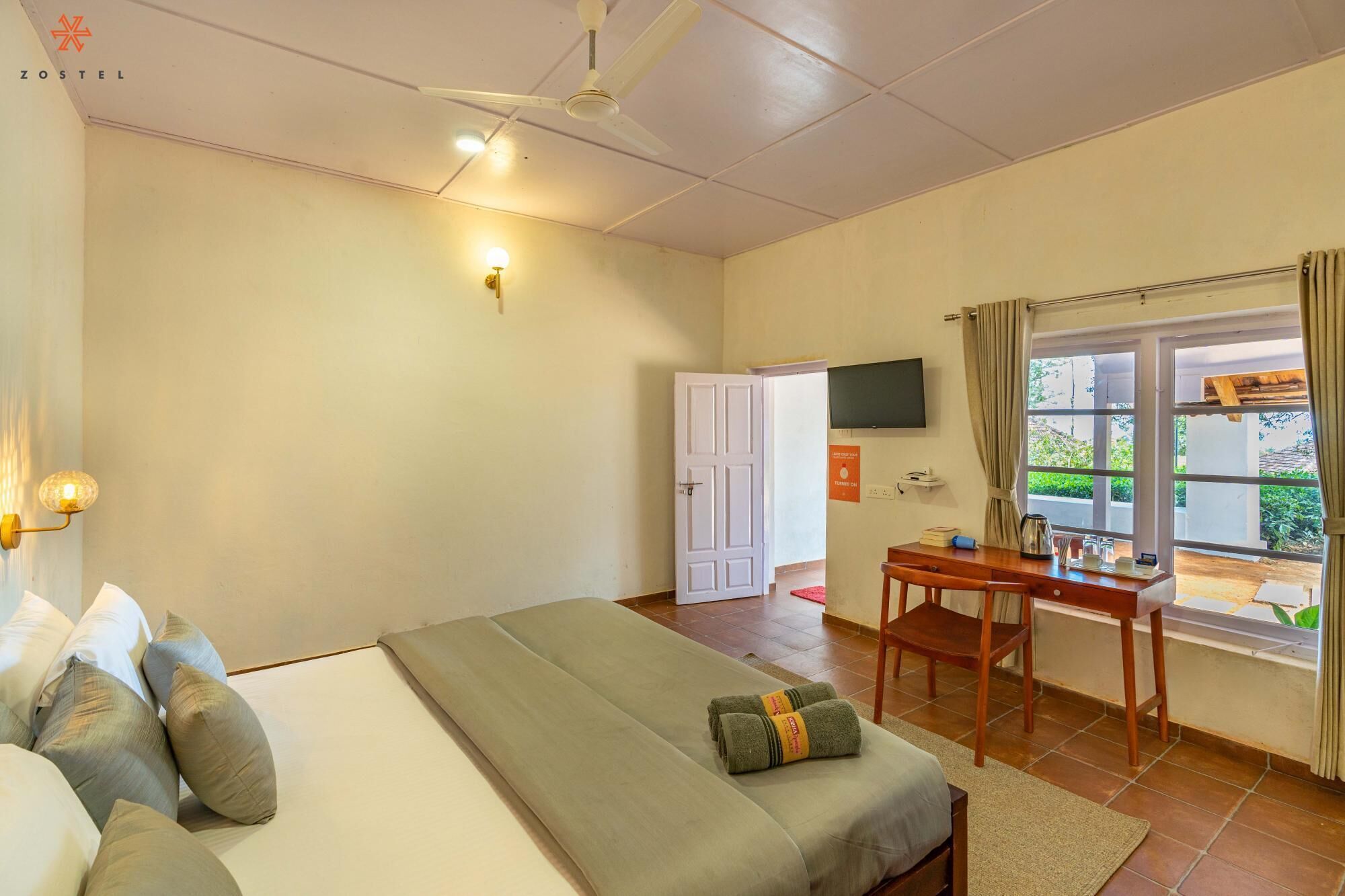 A bedroom with a bed, a desk, a chair, a TV, and a window with curtains.