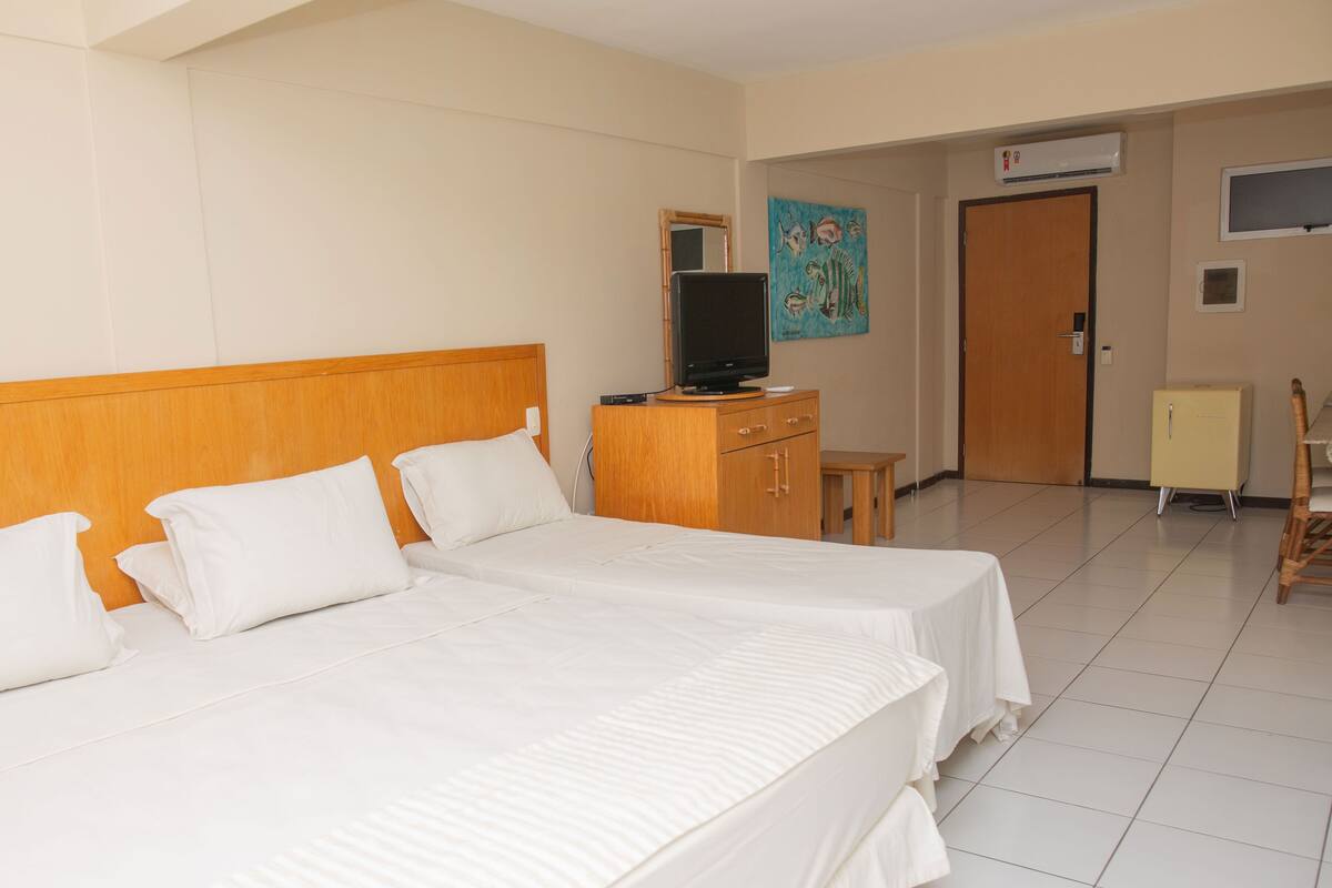 A hotel room with two beds, a television, a small cabinet, and a door leading to another room.