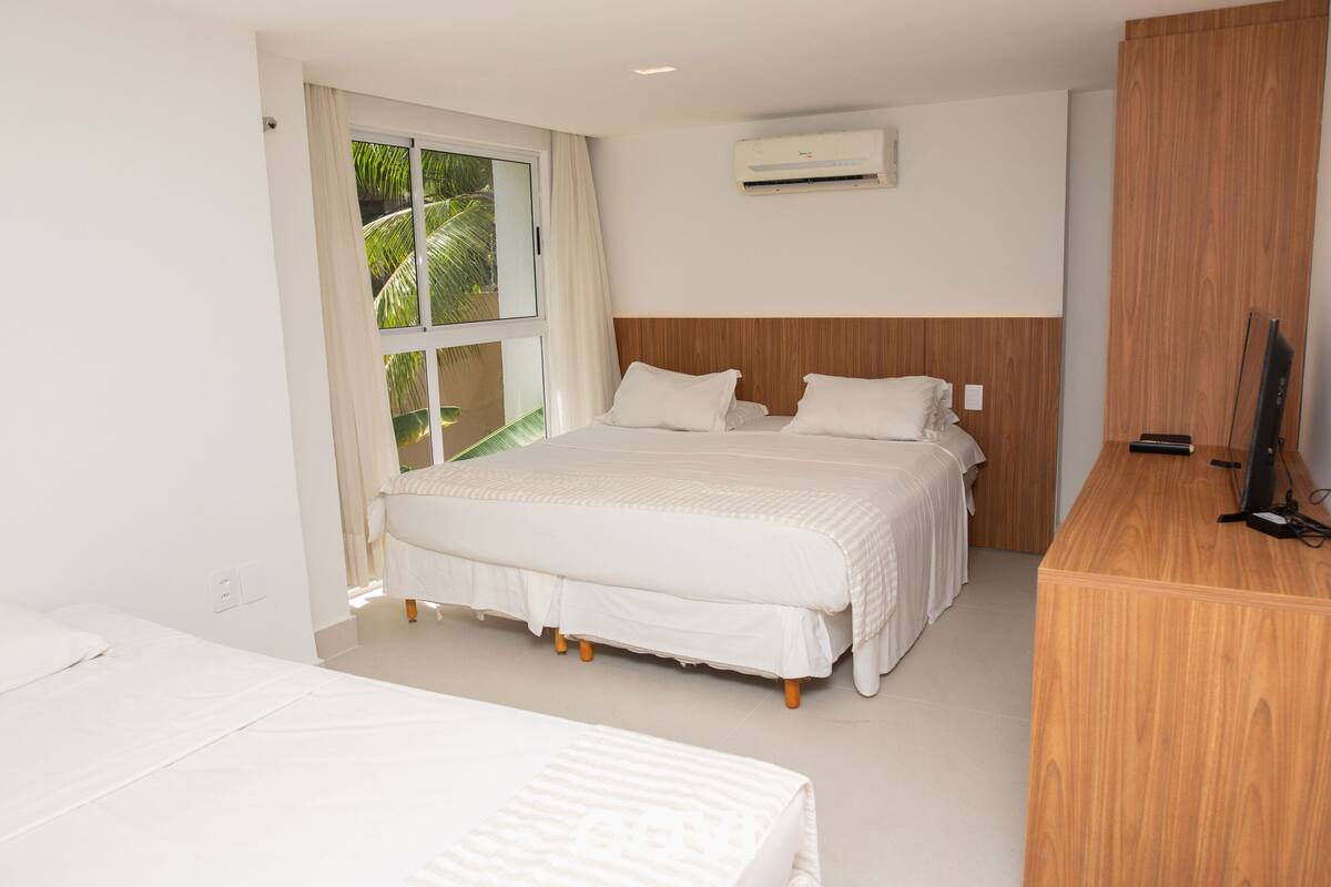 A hotel room with a large bed, a wooden headboard, a TV, and a window with curtains.