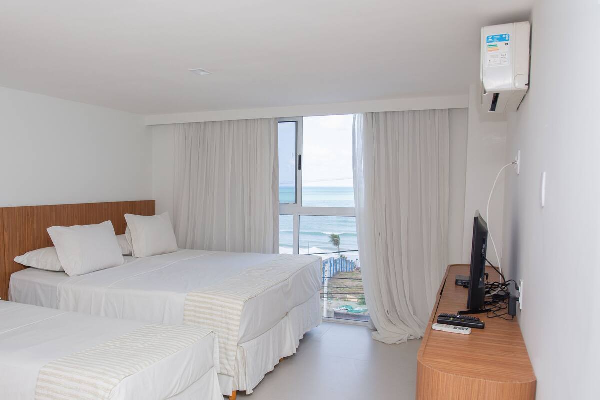 A hotel room with two beds, a wooden headboard, a TV, and a view of the ocean.