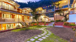 A hotel with multiple buildings, outdoor seating, and a stone pathway. - Zostel Plus Kareri (Dharamshala)