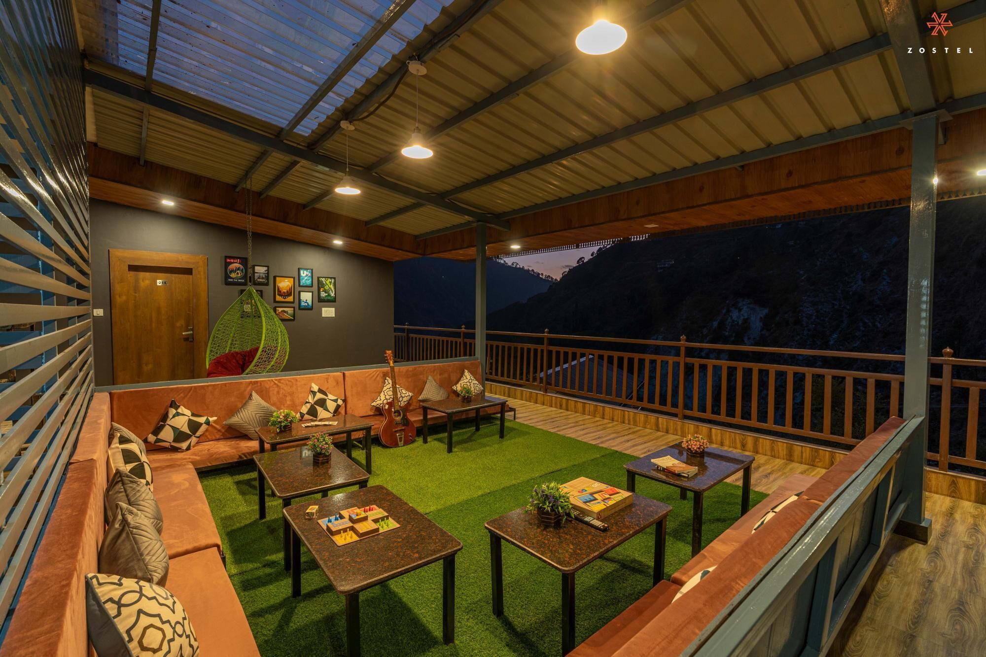A cozy lounge area with a wooden ceiling, a hanging chair, and a view of the mountains.