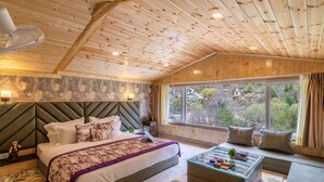 A wooden cabin bedroom with a bed, bedside table, lamp, and a view of the outdoors. - Zostel Plus Kareri (Dharamshala)
