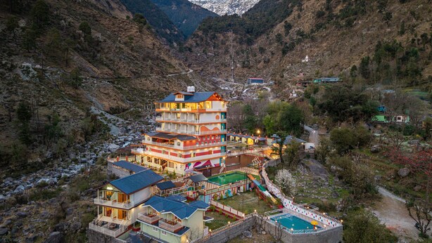A multi-story hotel with balconies, a swimming pool, and a view of the surrounding mountainous terrain. - Zostel Plus Kareri (Dharamshala)