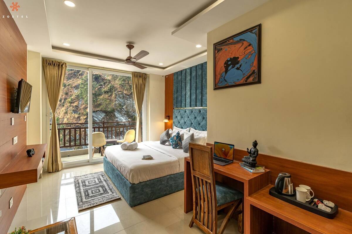 A modern hotel room with a large bed, a desk with a laptop, a coffee maker, and a view of the outdoors.