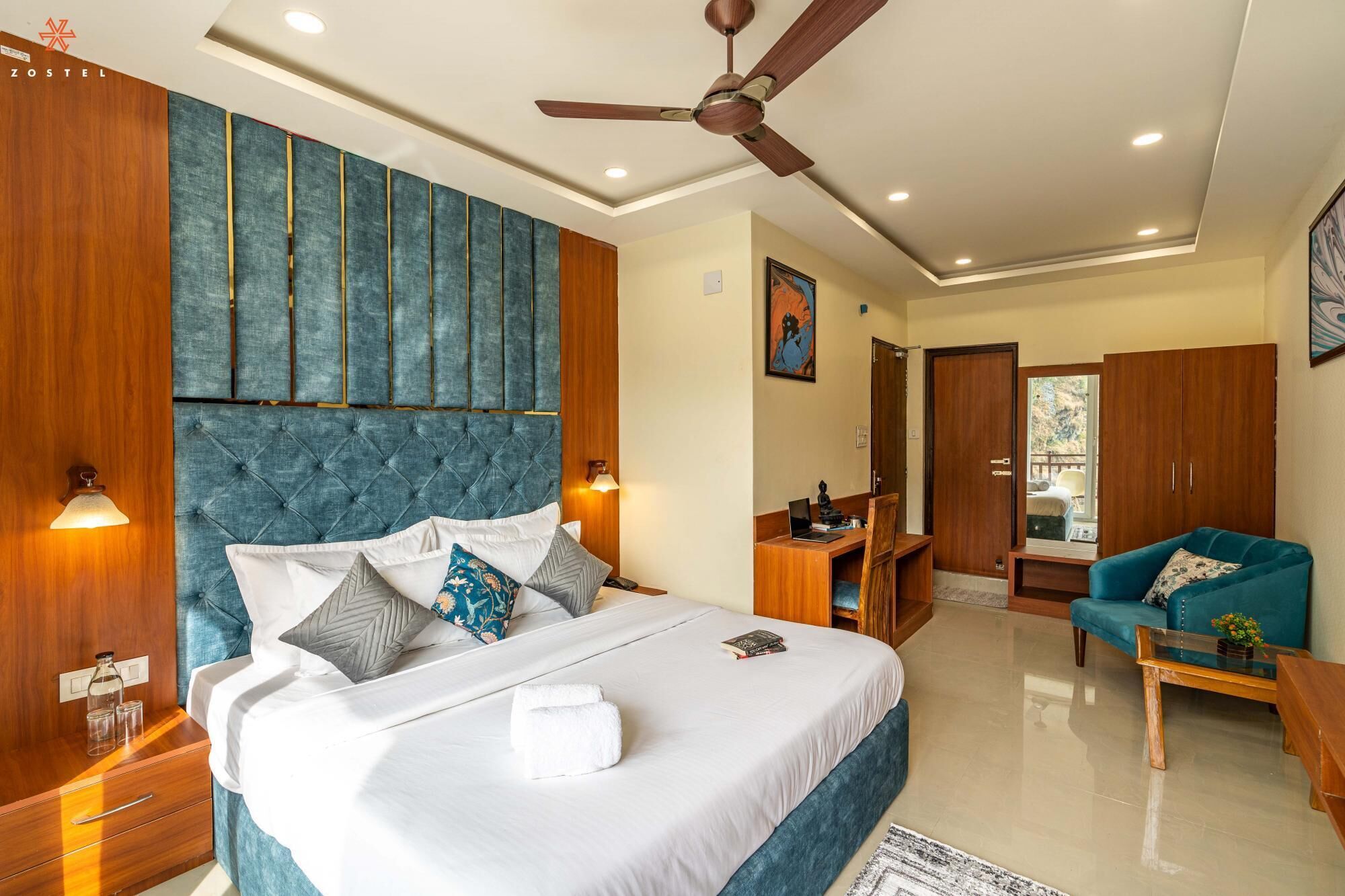 A modern bedroom with a tufted headboard, a ceiling fan, a desk, and a sofa.