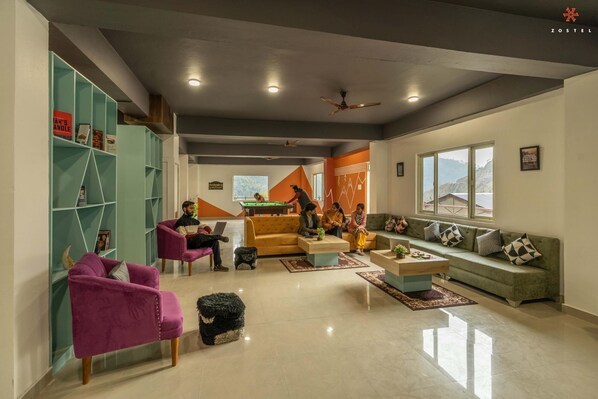 A modern living room with a pool table, a sofa set, and a teal bookshelf.