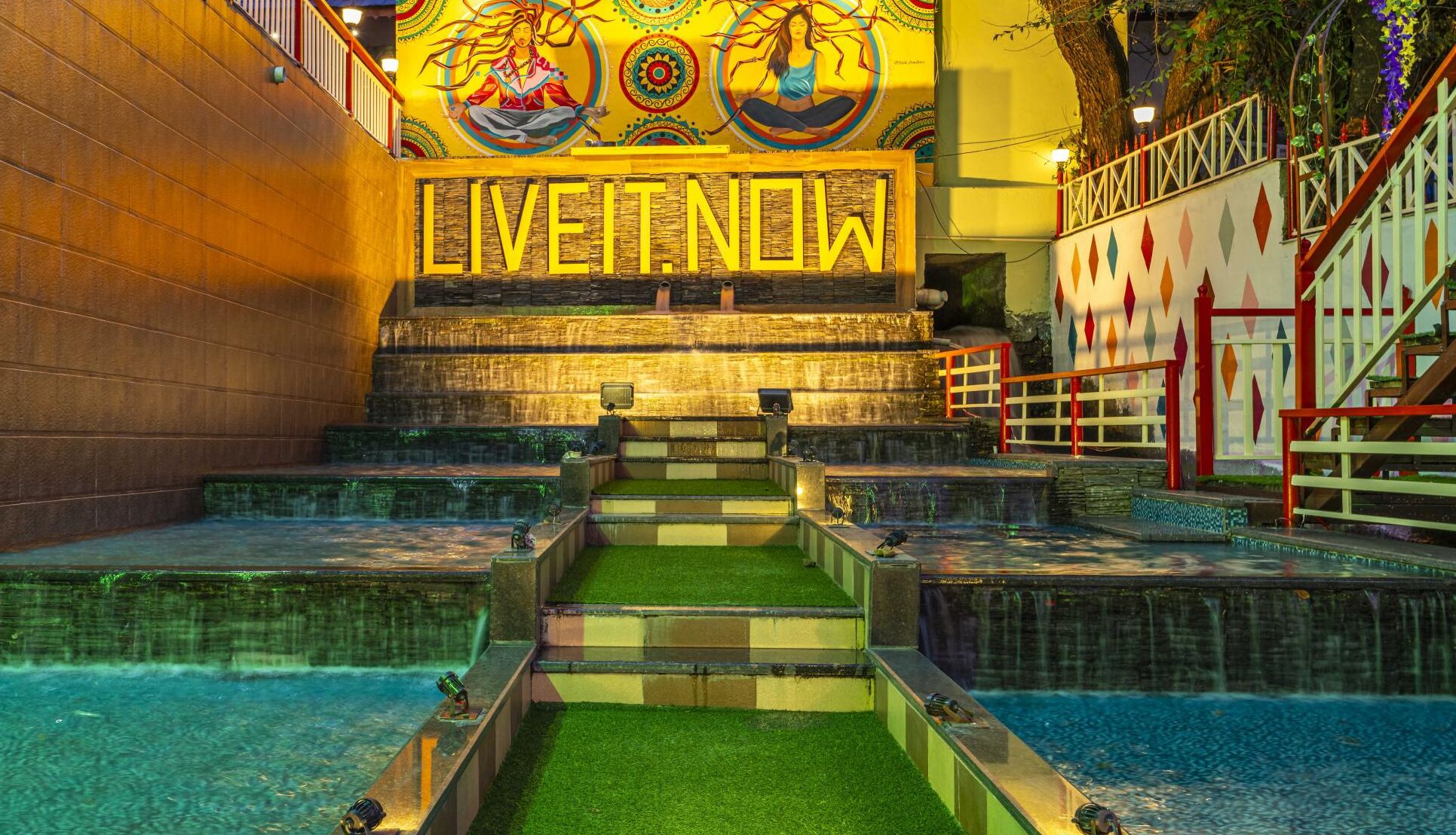 Ein Wellnessbereich mit einer großen Wandmalerei, einer Treppe, die zu einem Pool führt, und einem Schild mit der Aufschrift 'LIVE NOW'.