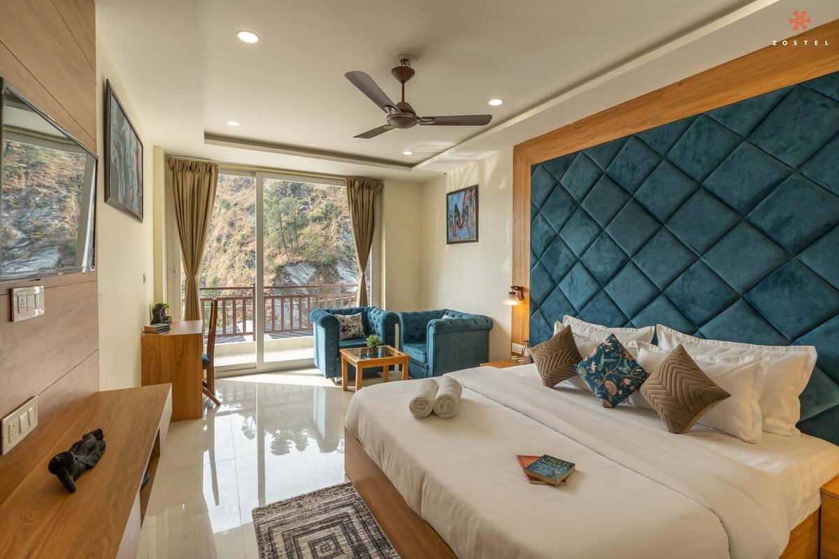 A modern hotel room with a large bed, a ceiling fan, a balcony with a view of the outdoors, and a wooden desk.