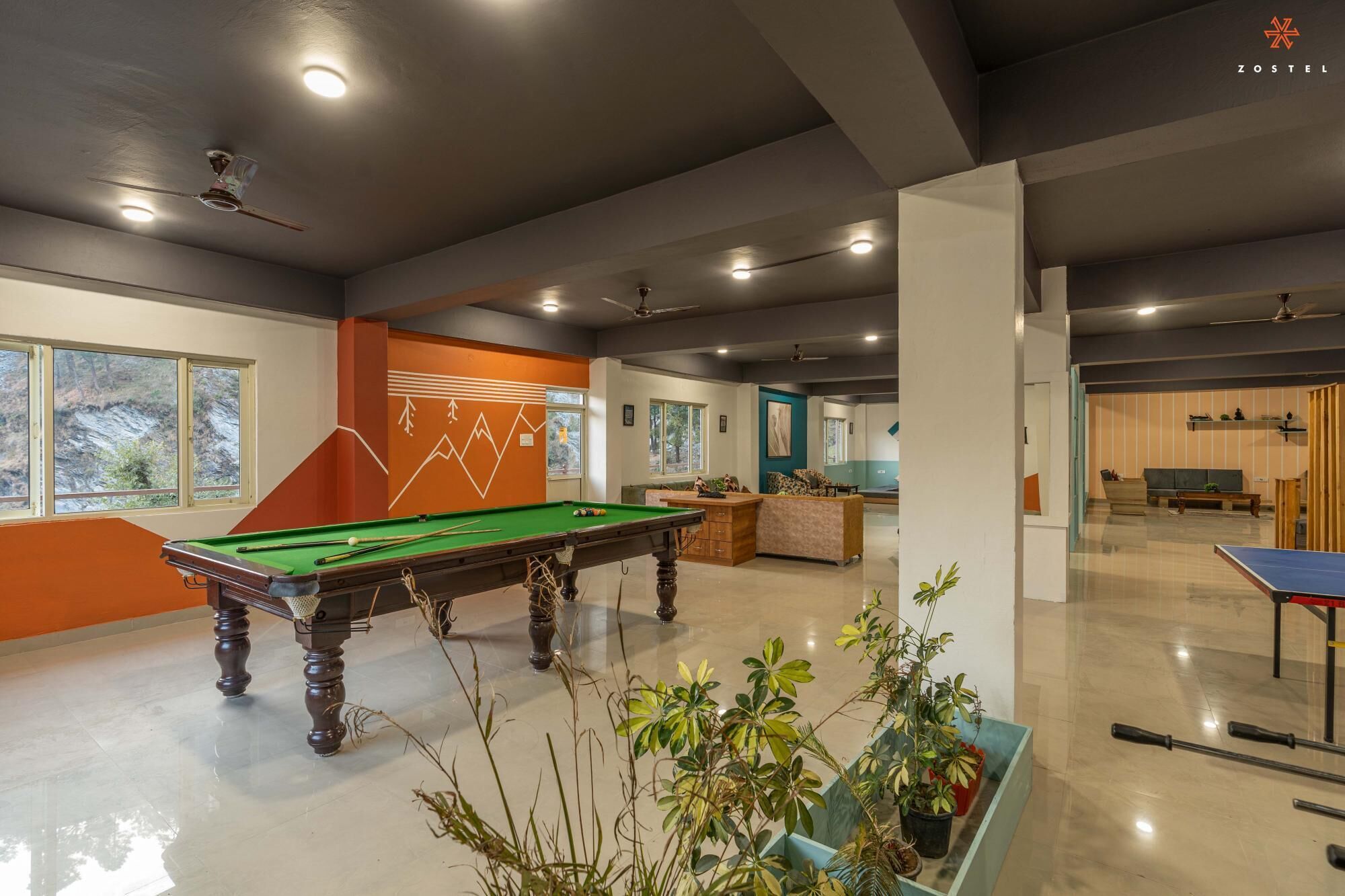 A pool table in a room with a large window, a sofa, and a ping pong table.