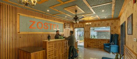 A reception area with a wooden reception desk, a sign reading "ZOSTEL", and a ceiling fan.