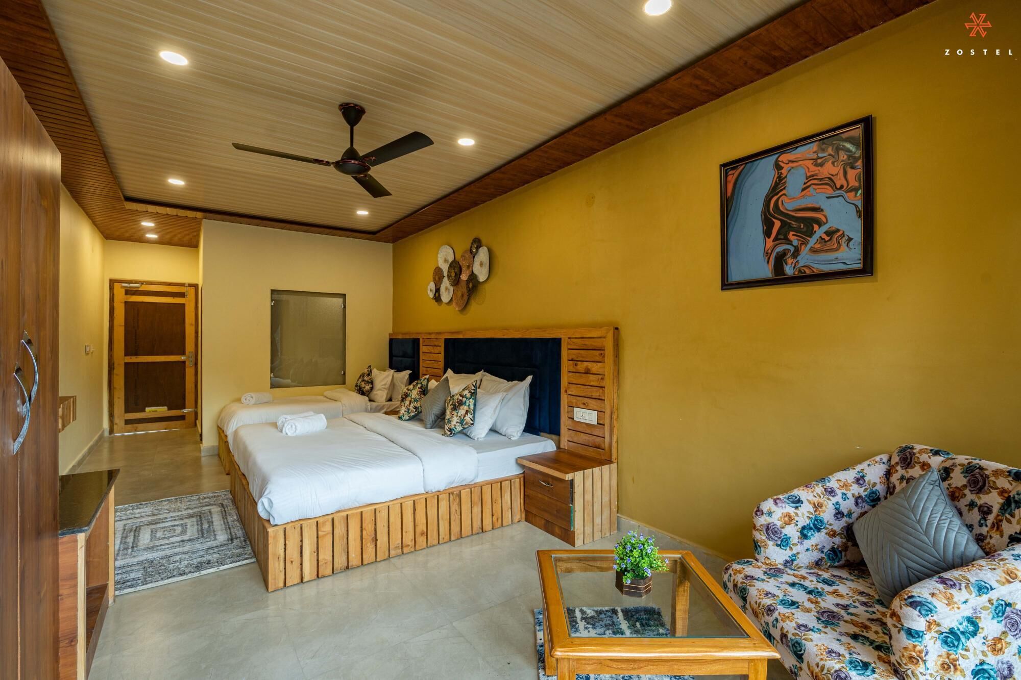 A hotel room with a large bed, a sofa, a coffee table, and a ceiling fan.
