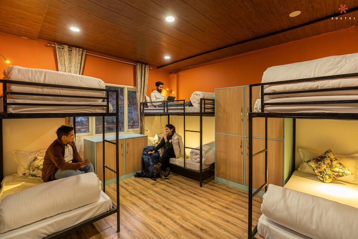 A dormitory room with bunk beds, wooden floors, and orange walls.