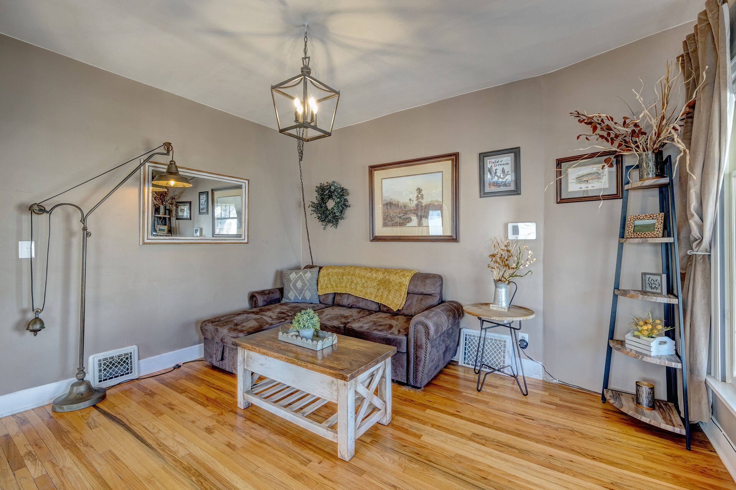 A cozy living room with a brown leather sofa, a wooden coffee table, a floor lamp, and a bookshelf.